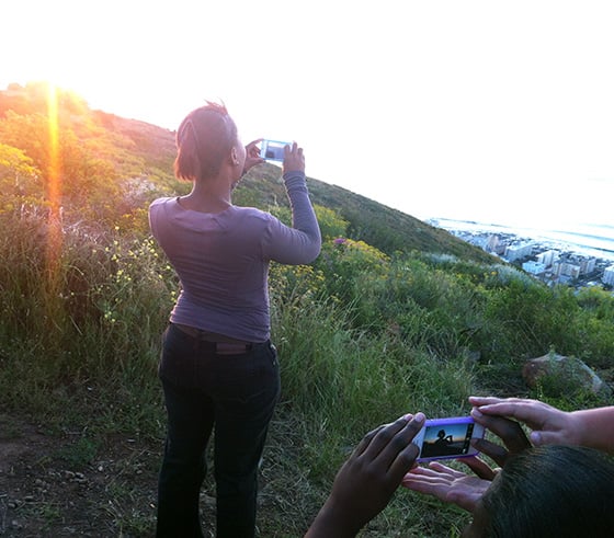 Ntombebhongo Pikoli poses as I teach the ladies how to photograph a silhouette on Sunset Hill in Cape Town, South Africa. My hands are pictured with Nwabisa Ndongeni’s hands. Photo by Aviwe Dalingozi.