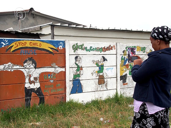 Yolanda Nkatula captures a photo of ‘ Stop Child Abuse’ and ‘Stop Woman Abuse’ murals in Khayelitsha, South Africa. Photo by Andrea Rees.